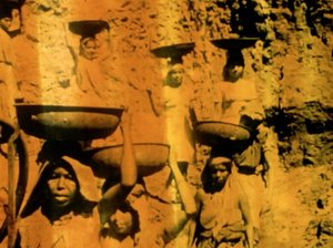 golden toned image of people outdoors carrying large bowls on their heads