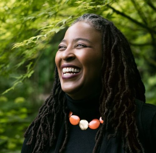 Camille Dungy smiles, wearing black top against a background of green trees