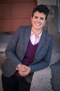 Jamie Manson in suit jacket, shirt and vest, smiling, leaning against stair rail