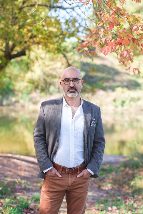 John Ghazvinian stands on a leafy bath with trees overhead