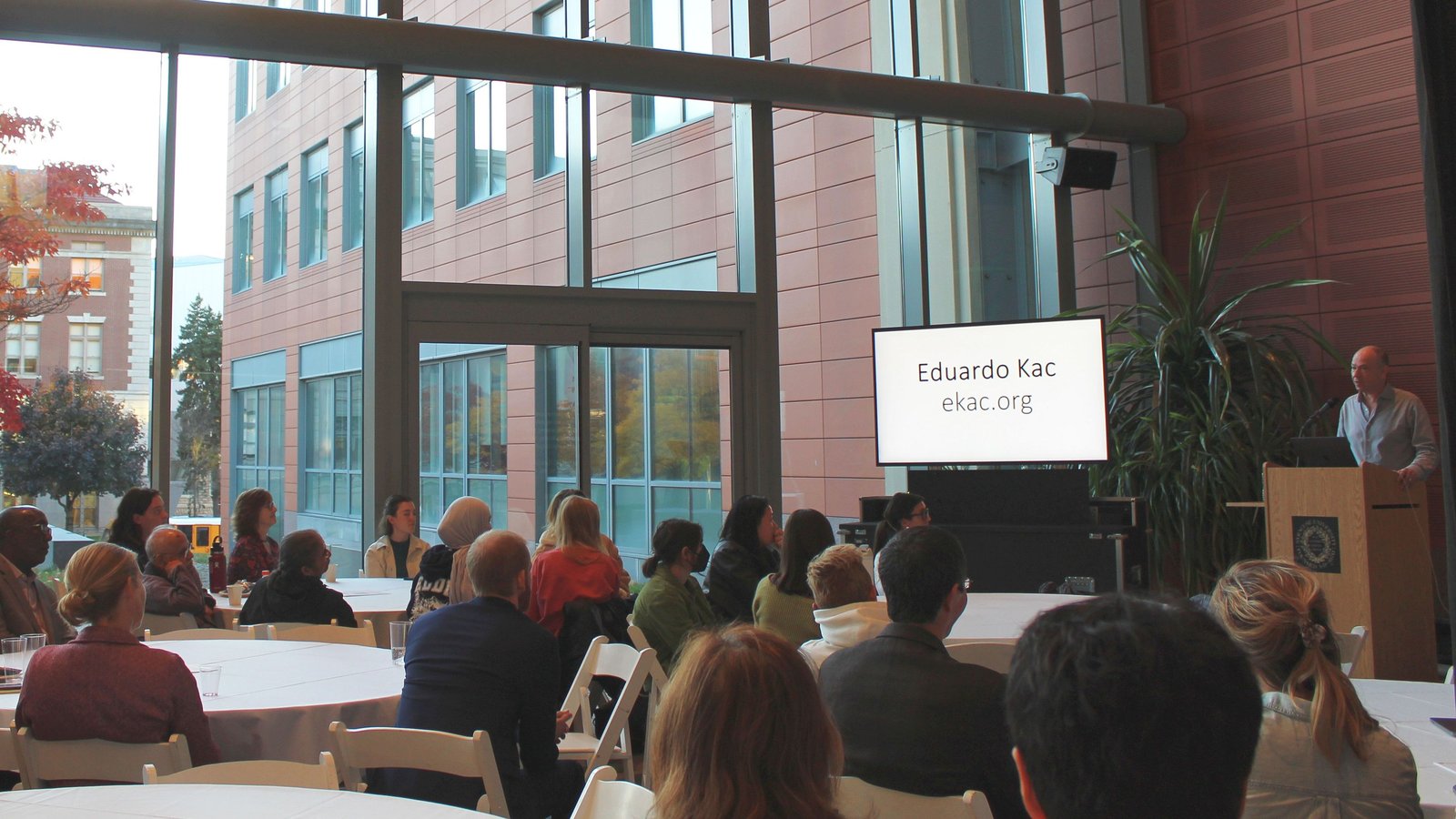 Eduardo Kac lectures an audiences seated at round tables