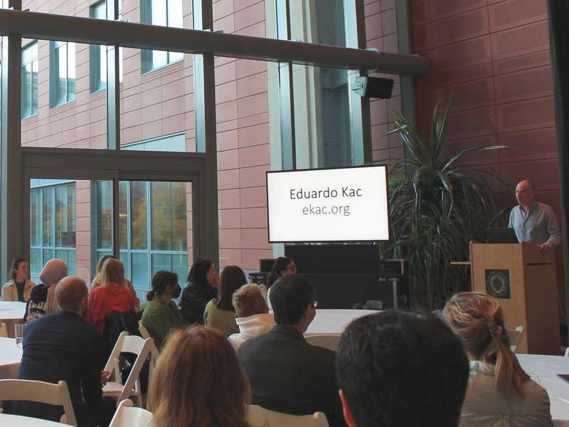 Eduardo Kac lectures an audiences seated at round tables