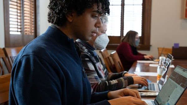 three people seated at table type onto their laptops