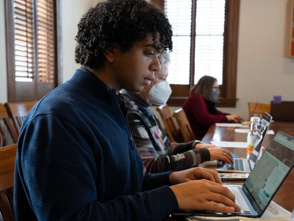 three people seated at table type onto their laptops