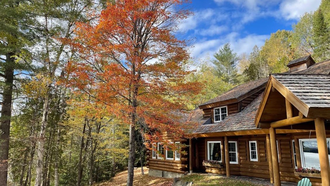 view of rustic cabin beyond fall-colored trees