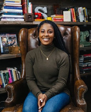 Sara trail sits on a leather chair in front of bookshelves