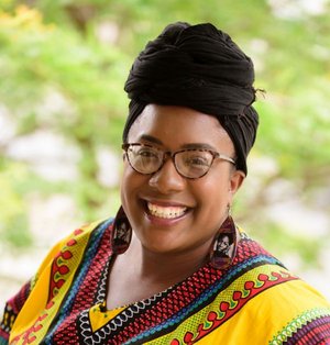 Sequoia Kemp in multi-colored top and black headscarf, smiling against leafy green background