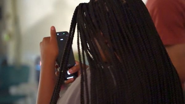 over-the-shoulder look at a black-haired student examining the contents of their cell phone screen