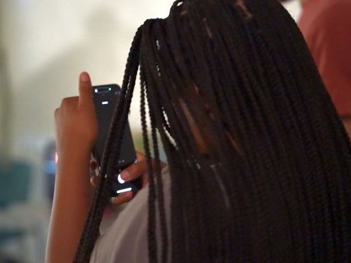 over-the-shoulder look at a black-haired student examining the contents of their cell phone screen