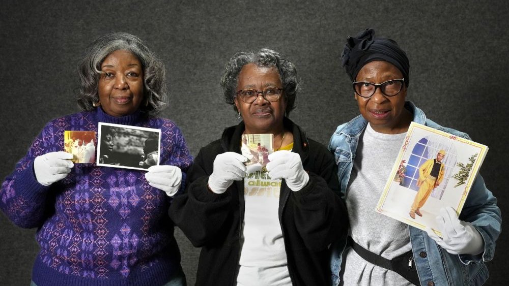 three women hold up old photographs in their gloved hands