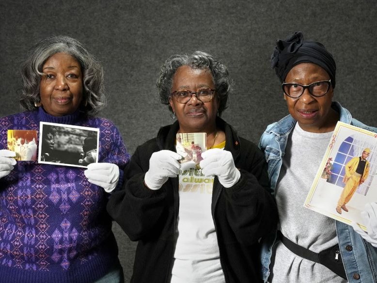 three women hold up old photographs in their gloved hands