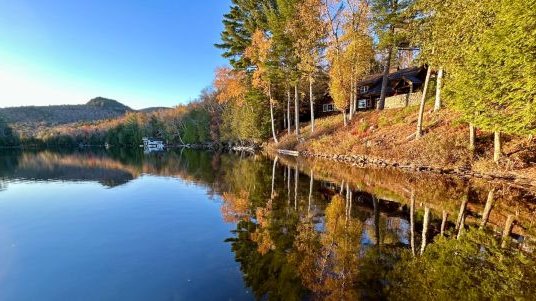 glassy blue lake rimmed by fall leafed trees and mountains in the distance