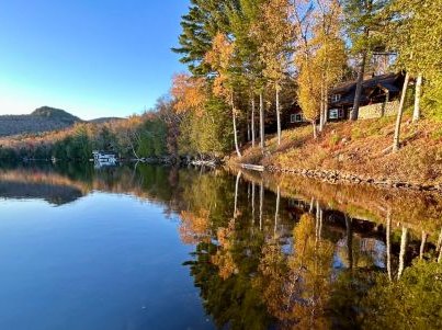 glassy blue lake rimmed by fall leafed trees and mountains in the distance